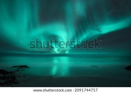 Aurora borealis over the sea. Northern lights in Lofoten islands, Norway. Starry sky with polar lights. Night landscape with aurora, sea with blurred water and sky reflection, sandy beach. Aurora 