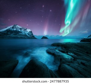 Aurora borealis over the sea, snowy mountains at starry winter night. Northern Lights in Lofoten islands, Norway. Sky with polar lights. Landscape with aurora, rocky beach, sky, reflection in water - Powered by Shutterstock