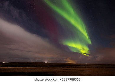 Aurora borealis over snow covered hillside in wintery surroundings. Icelandic northern lights are magnificent spectacle of nature, shining the nighttime sky in an icy landscape.