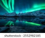 Aurora borealis over the snowy mountains, frozen sea, reflection in water at winter night. Lofoten, Norway. Northern lights and snowy rocks. Landscape with polar lights, starry sky and fjord. Scenery