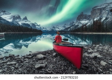 Aurora borealis over Spirit island with female traveler sitting on red canoe on Maligne Lake at Jasper national park, AB, Canada
