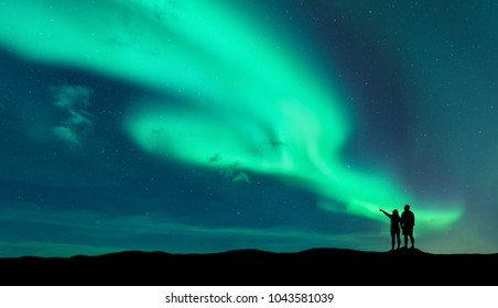 Aurora borealis and silhouette of standing man and woman who pointing finger on northern lights. Lofoten islands,Norway. Aurora. Sky with stars and polar lights. Night landscape with aurora and couple - Powered by Shutterstock