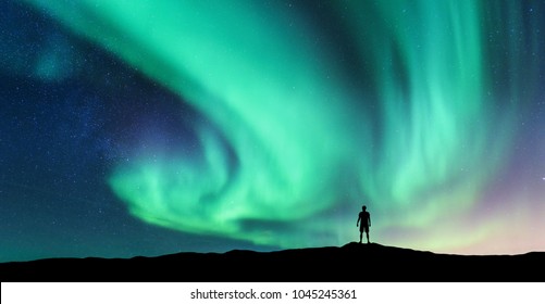 Aurora borealis and silhouette of standing man. Lofoten islands, Norway. Aurora and happy man. Sky with stars and green polar lights. Night landscape with aurora and people. Concept. Nature background