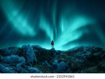 Aurora borealis and young woman on mountain peak at night. Northern lights, stones and silhouette of alone girl on mountain trail. Landscape with polar lights. Starry sky with bright aurora. Travel - Shutterstock ID 2352941861