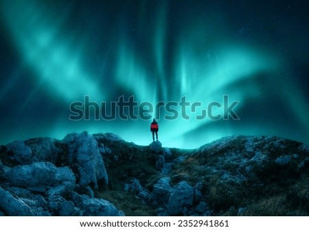 Aurora borealis and young woman on mountain peak at night. Northern lights, stones and silhouette of alone girl on mountain trail. Landscape with polar lights. Starry sky with bright aurora. Travel