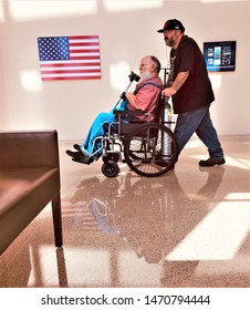 Aurora, CO, USA. Aug 2, 2019. Young man pushing his disabled veteran father in a wheel chair to his next medical appointment at the new VA Medical Center Hospital in Aurora, Colorado. 