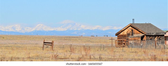 Aurora, CO, USA. March 2, 2020. Old Pioneer Log Cabin On The Grassy Plains Outside Of Denver With The Rocky Mountains In The Background. 