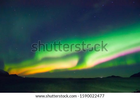 Aurora with muliple colors in green, orange and pink. Burst in the middle of Norwegian sea.