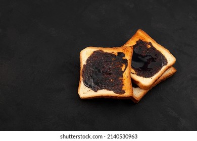 Aussie savory toasts for breakfast with vegemite (thick Australian healthy food spread made from leftover brewers yeast extract). Dark background, copy space.