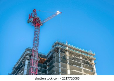 Austin, Texas- Under construction high-rise building with tower crane in a low angle view. There is a red tower crane at the front of the building with safety netting at the front.