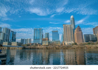 Austin Texas Urban Landscape With Buildings Along The Calm Colorado River. Waterfront Apartments And Offices Reflected On The Water With Blue Sky And Clouds Overhead.