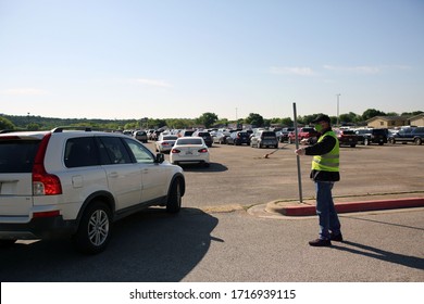 Austin, TX / USA - Apr. 15, 2020: A Male Volunteer Directs A Line Of Cars Into The Parking Lot Of A High School To Receive Emergency Food Aid From The Central Texas Food Bank.