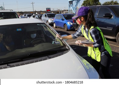 Austin, TX / USA - Apr. 15, 2020: A Female Volunteer Marks The Windshield Of A Car In A Line Of Cars In The Parking Lot Of A High School To Receive Emergency Food Aid From The Central Texas Food Bank.