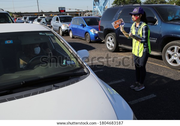 Austin, TX / USA - Apr. 15, 2020: A female\
volunteer offers census info to a woman in a line of cars in the\
parking lot of a high school to receive emergency food aid from the\
Central Texas Food\
Bank.