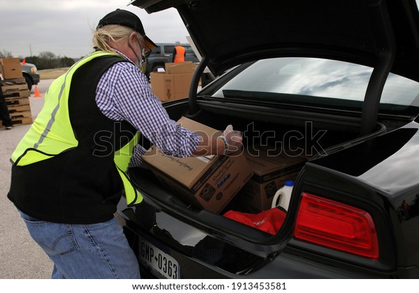 Austin, TX USA - Feb. 4, 2021: A male 
volunteer distributes emergency food aid from the Central Texas
Food Bank to people in need at the Exposition
Center.