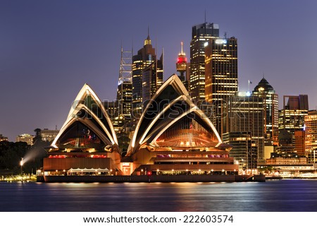 Australia iconic SYdney city landmarks CBD harbour and famous buildings greatly illuminated at sunset with reflection in still blurred harbour waters backgrounded by high-rises