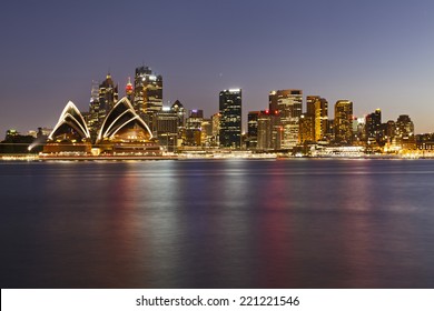 Australia Sydney City CBD Landmarks View Over Harbour At Sunset With Illumination And Blurred Lights Reflecting In Still Water