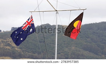 Australian and Aboriginal flags flutter from a white mast against a hilly landscape.