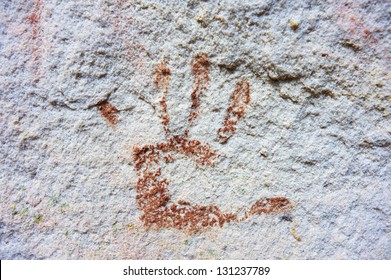 An Australian Aboriginal hand print using red ochre on a white rock wall.
