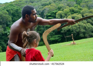 Australian Aboriginal warrior man teaching young Australian girl (female age 05) how to throw a boomerang during a cultural show in far tropical north of Queensland, Australia.