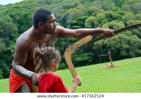 Australian Aboriginal warrior man teaching young Australian girl (female age 05) how to throw a boomerang during a cultural show in far tropical north of Queensland, Australia.
