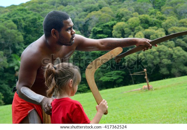 Australian Aboriginal\
warrior man teaching young Australian girl (female age 05) how to\
throw a boomerang during a cultural show in far tropical north of\
Queensland,\
Australia.