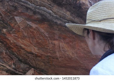 Australian Adult Woman Tourist Looking At Prehistoric Australian Aboriginal Art Cave Painting At Ubirr Rock Art Site In Kakadu National Park Northern Territory Of Australia.