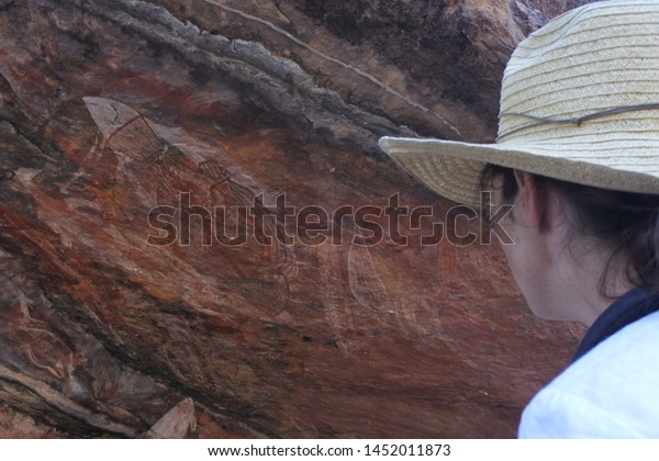 Australian adult woman\
tourist looking at prehistoric Australian aboriginal art cave\
painting at Ubirr rock art site in Kakadu National Park Northern\
Territory of\
Australia.