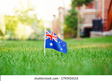 Australian Flag Standing On Green Grass In Front Of House. Australia Day National Holiday Celebration. Nature Background Outdoor. Real Estate Property In Australia.