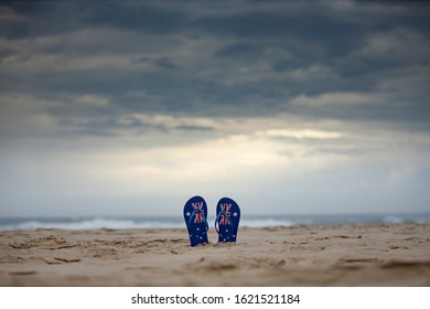 Australian flag thongs sticking upright in sand on an Aussie beach with dramatic storm clouds background. Australia day and waiting for rain concept.