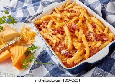 Australian Fries Smothered In Melted Mix Of Shredded Cheese And Bacon In A Baking Dish On A White Wooden Table With Ingredients At The Background, View From Above, Close-up