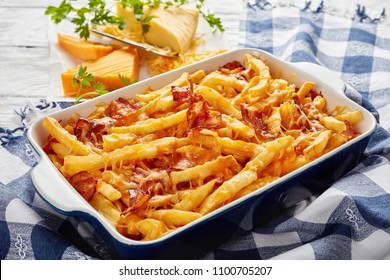 Australian Fries Smothered In Melted Mix Of Shredded Cheese And Bacon In A Baking Dish On A White Wooden Table With Grated Cheese At The Background, View From Above, Close-up