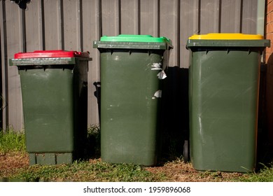 Australian garbage wheelie bins with red and yellow lids for general and recycling household waste and green lid for garden waste near the resedential building.