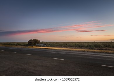Australian outback landscape, multi-lane highway with colorful clouds at dusk.