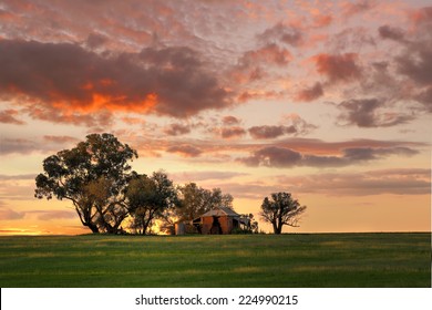 Australian Outback Sunset.  Old Farm House, Crumbling Walls And Verandah W Sits Abandoned On A Hill At Sunset. The Last Sun Rays Stretching Across The Landscape Painting The Grass In Dappled Light 