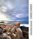 Australian rocky coastline and a sheltered cove in the Bay of Fires in Tasmania with lichen covered boulders and blue sky with a few clouds over the southern ocean and the beach in the background