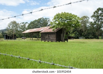 Australian Rural Landscape, Old Farm Shed In Field Beyond The Barbed Wire Fence.