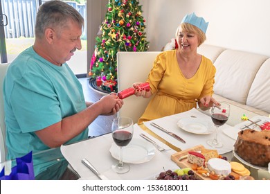 Australian Senior Couple Pulling Christmas Cracker While Sitting Behind Dressed Table Before Dinner