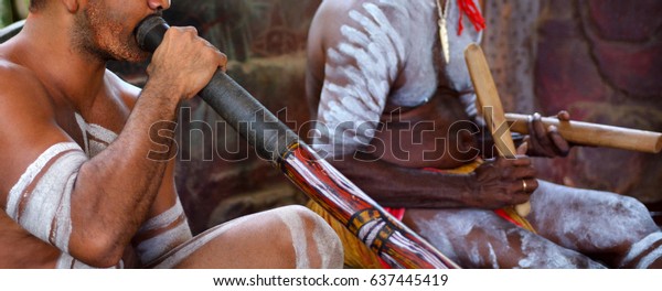 Australians Aboriginal men playing\
Aboriginal music on didgeridoo and wooden sticks in a culture\
ceremony festival event in the Far North Queensland,\
Australia.