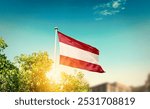 Austria national flag waving in blue sky behind the tree and building. The flag blowing with beautiful sunlight. Austria national flag for independence day.