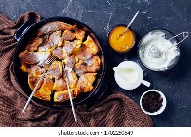 Austrian Sweet Pancake Kaiserschmarrn With Applesauce, Raisins And Powdered Sugar, Golden Cutlery On A Black Baking Dish On A Dark Concrete Background, Top View, Flat Lay