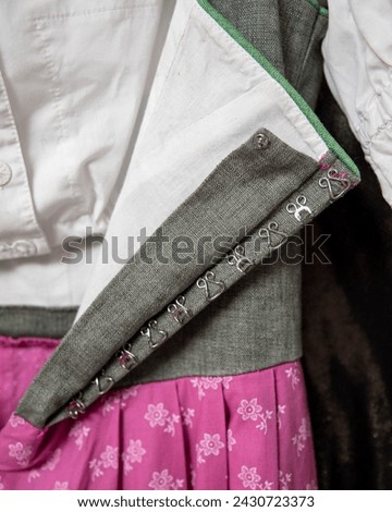 Austrian traditional dirndl with low neckline, close up. Grey bodice, pink skirt having floral pattern print, white cotton blouse and lining.  Row of sewed fasteners: hooks and eyes type. Ethnic style