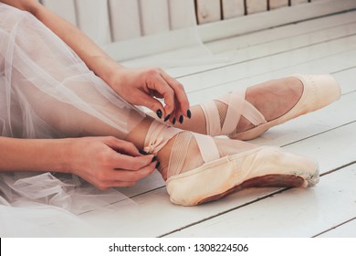 The Authentic Ballerina Ballet Dancer Sitting On The Floor And Tying Pointe Shoes, Close Up
