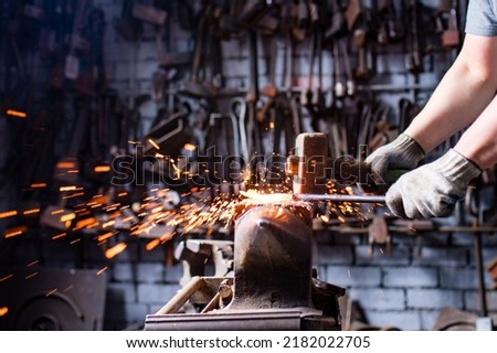 Authentic blacksmith man forges a metal product in dark indoors studio