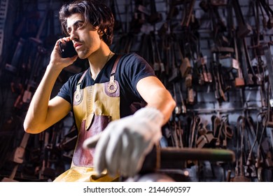 Authentic blacksmith man wear leather apron in dark indoors studio calling by phone - Powered by Shutterstock