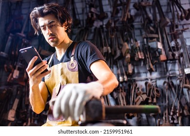 Authentic blacksmith man wear leather apron in dark indoors studio looking at phone screen - Powered by Shutterstock