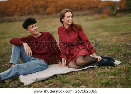 An authentic candid moment captures two people relaxing on a blanket in a sunlit autumn park, presenting genuine connection and a natural, unscripted mood.