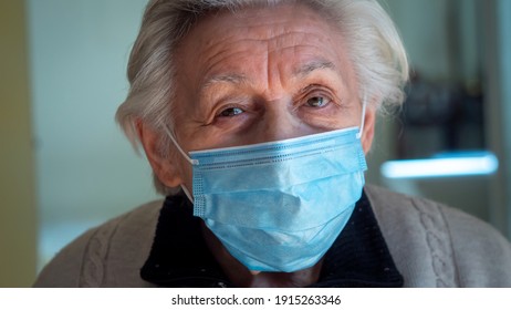 Authentic Cinematic Close Up Shot Of Retired Disabled Grey Hair Senior Woman With Protective Medical Mask Smiling In Camera At Home. Concept Of Covid-19, Healthcare, Protection,care For Older People.