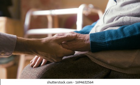 Authentic Close Up Shot Of An Young Man Is Holding Hands Of Disabled Senior Woman In Wheelchair As Sign Of Care And Support. Concept Of Family, Retirement, Life,boarding House, Help, Authenticity