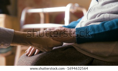 Authentic close up shot of an young man is holding hands of disabled senior woman in wheelchair as sign of care and support. Concept of family, retirement, life,boarding house, help, authenticity